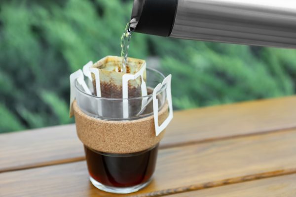 A 1085 Snowdonia Coffi drip coffee bag over a mug at a campsite.
